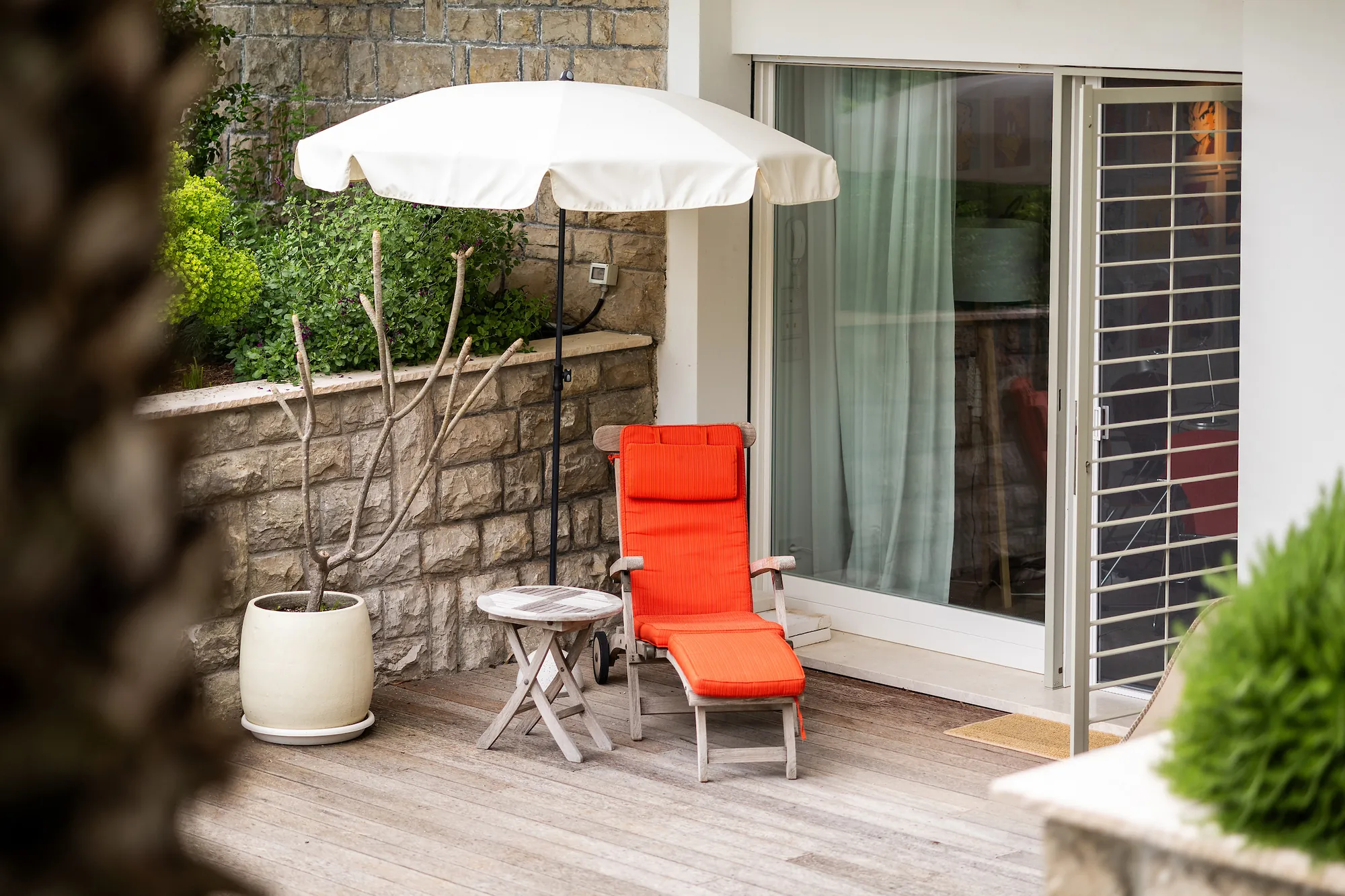 The Iroko-wood terrace of the garden apartment with a red lounger and parasol