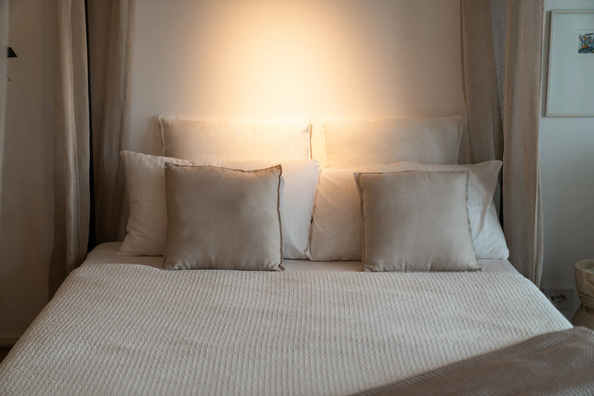 Soft linen cushions on a white bed in warm lamplight