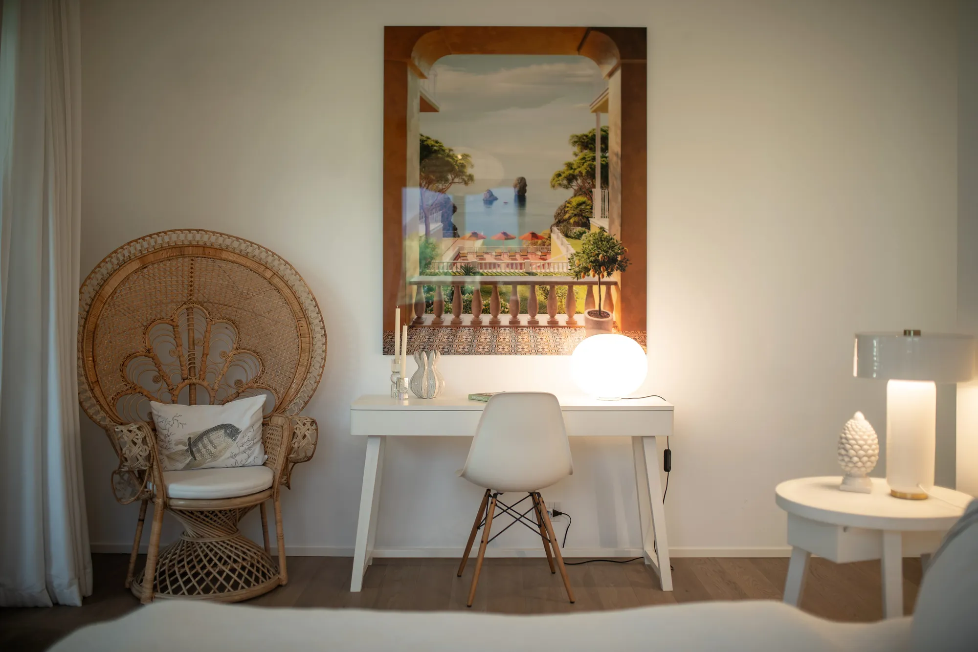 Writing desk with a rattan peacock chair and a vintage Riviera painting in a bedroom