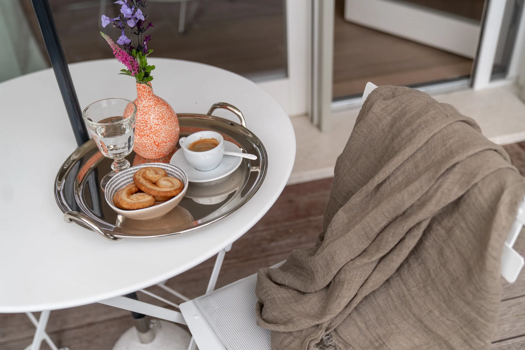 Coffee, biscuits and a small vase of flowers on a silver tray, a linen throw on the chair