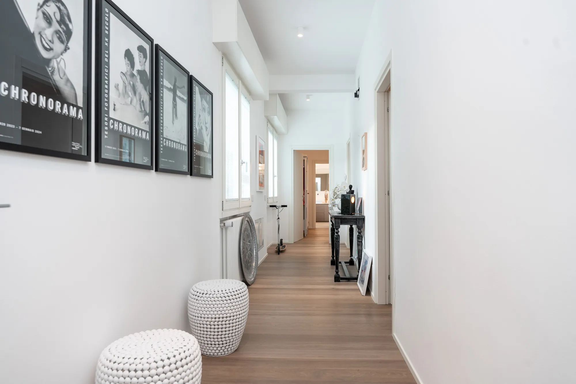 Bright corridor with oak parquet, white knitted stools and framed black-and-white vintage posters