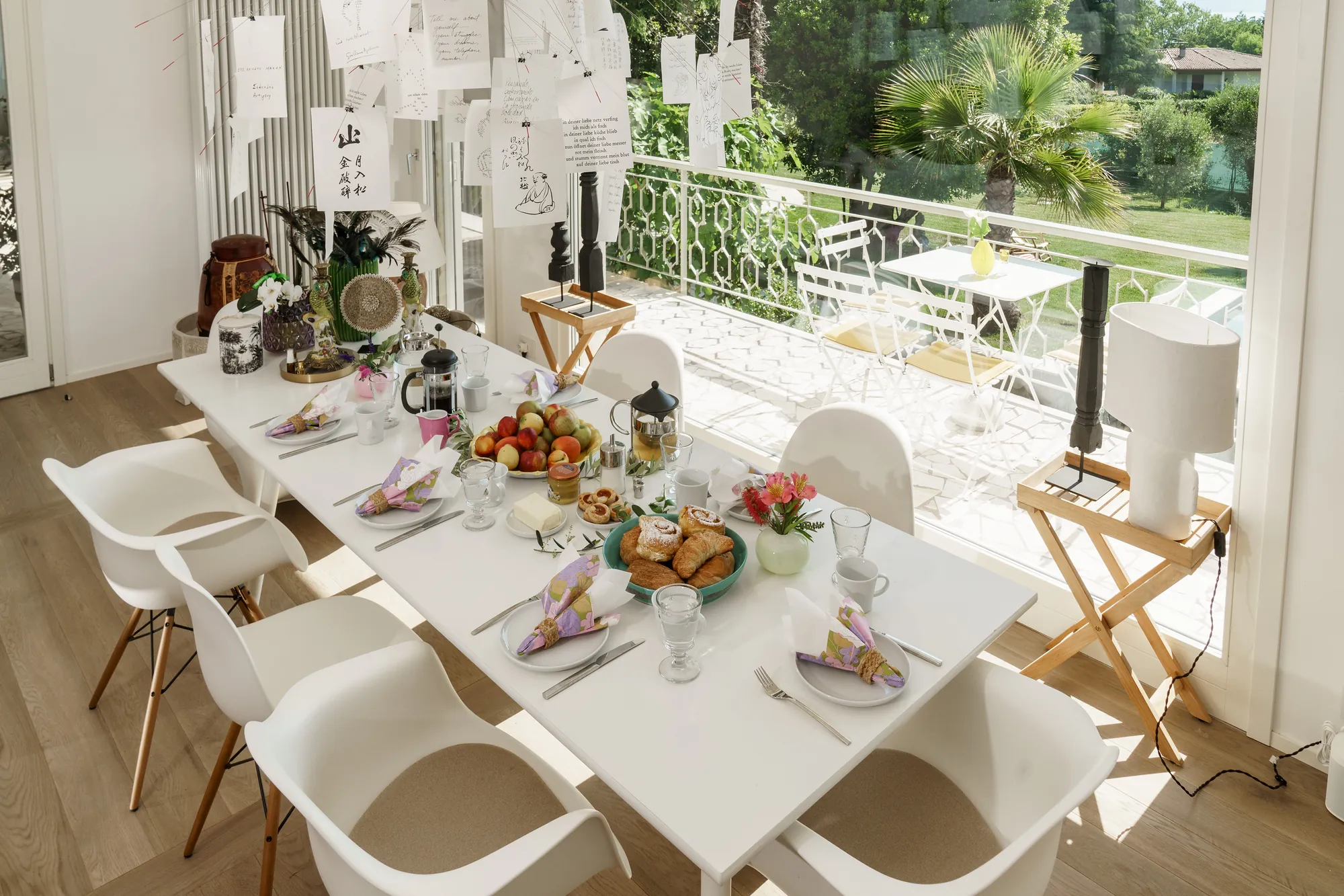 Breakfast laid on the white dining table beneath an Ingo Maurer Zettel'z paper-note chandelier