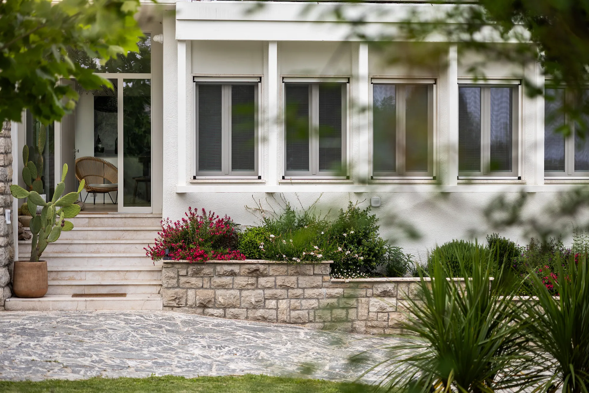 Marble entrance steps flanked by red flowers, cacti and a stone wall at the villa entrance