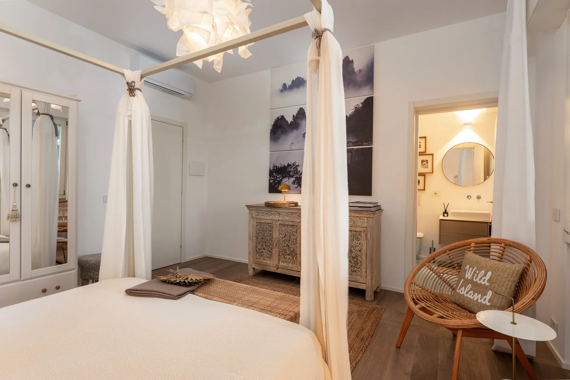 Four-poster bed with linen drapes and a rattan chair, the en-suite bathroom glimpsed through the door