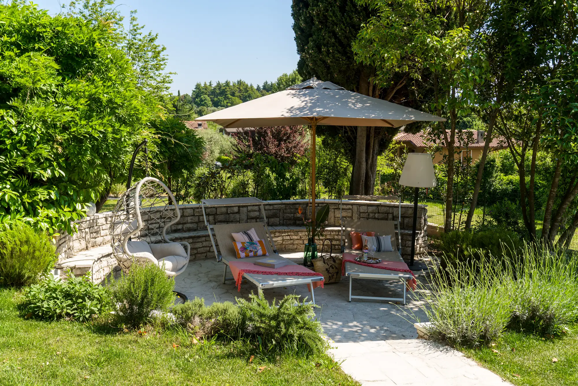 A secluded garden lounge with stone bench, hanging chair and parasol among lavender
