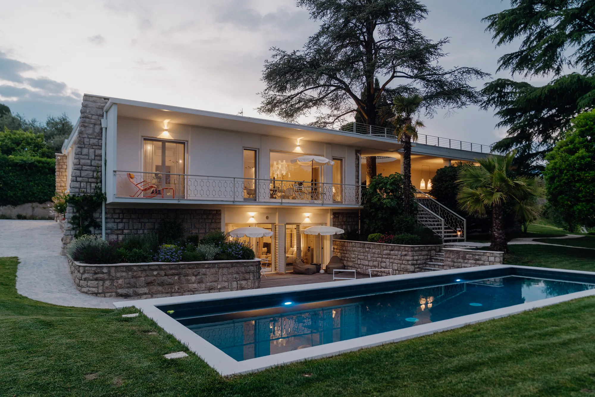 The white 1960s villa lit up in the evening, seen across the illuminated saltwater pool