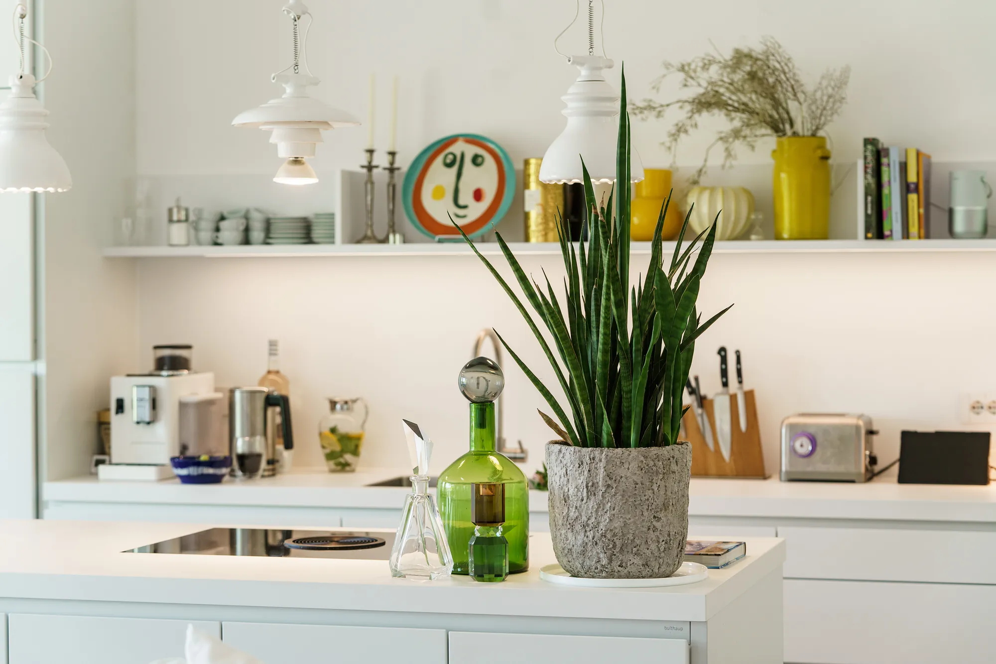 Kitchen detail with open shelves, ceramics, a green glass carafe and a potted plant