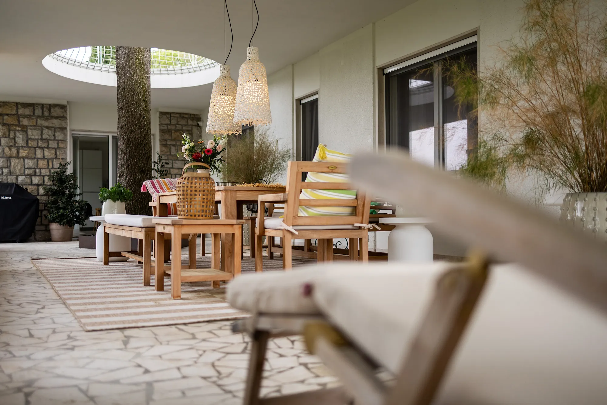 The main terrace with teak dining table, woven pendant lamps and the cedar trunk rising through the roof