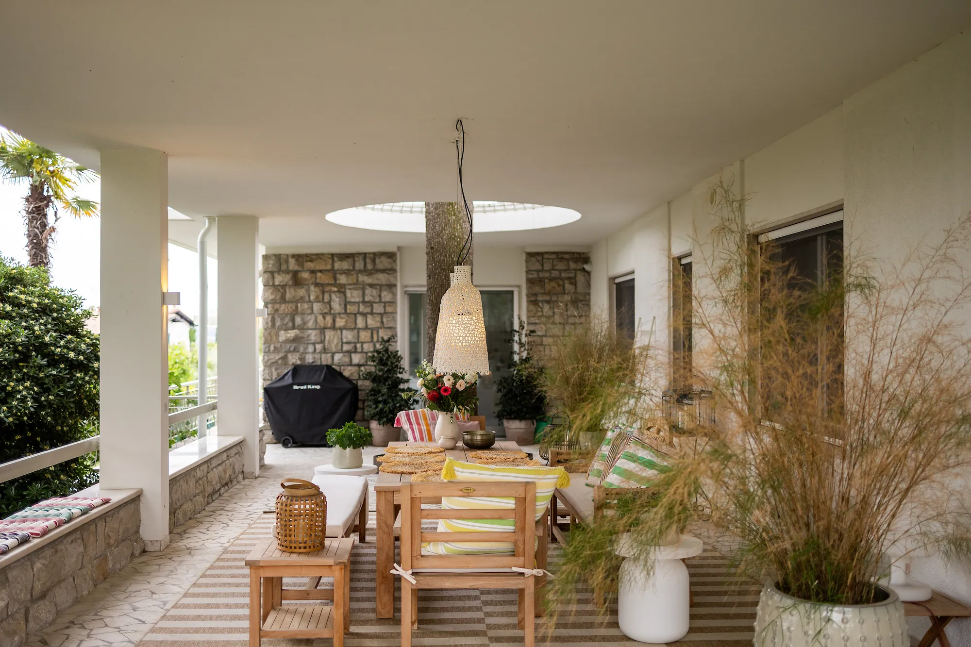 Overview of the covered marble terrace with teak furniture, lamps and the circular opening for the cedar