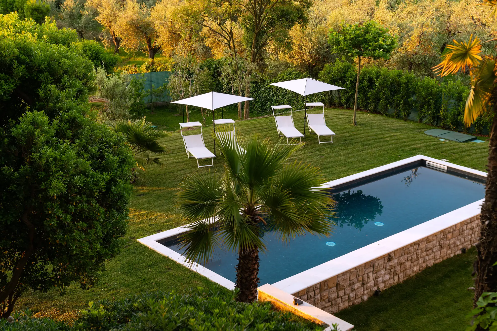 The pool and garden from above at golden hour, sun loungers and parasols on the lawn