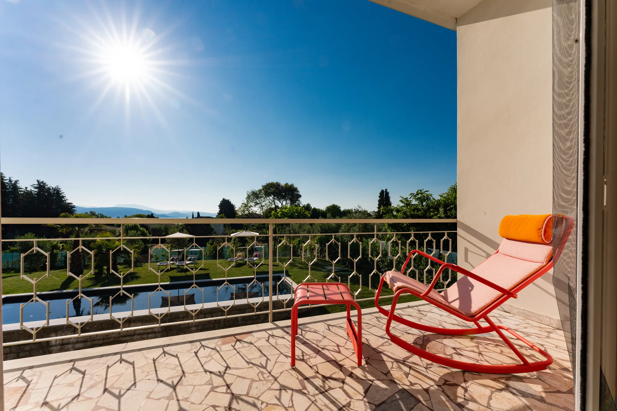 A red rocking chair on the sunny balcony overlooking the pool and garden