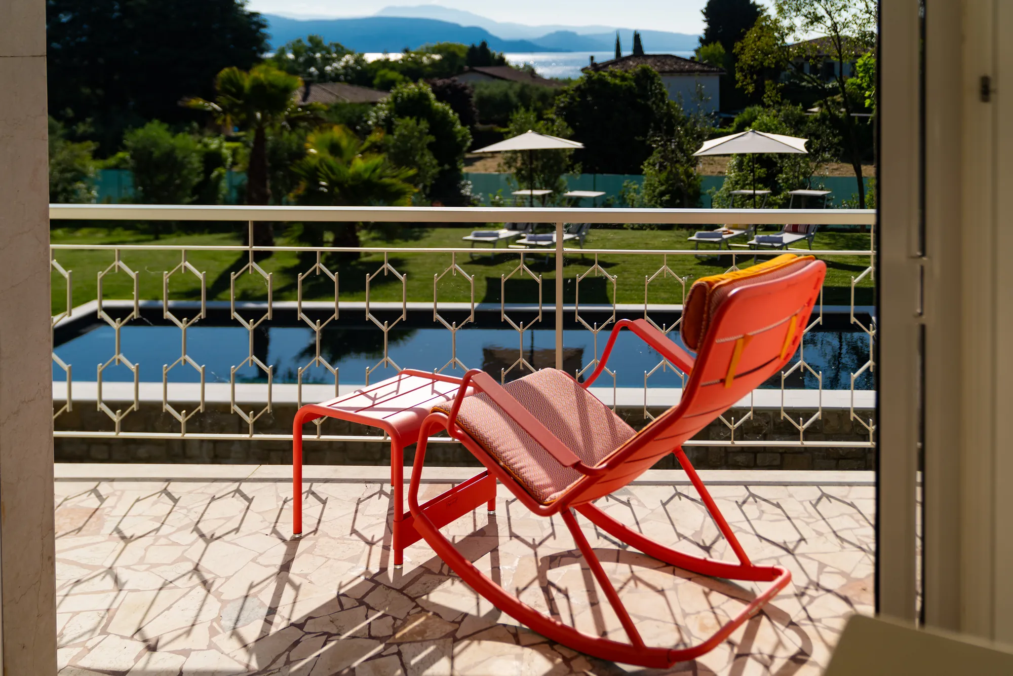 Red rocking chair on the patterned-tile balcony with the pool below and Lake Garda beyond