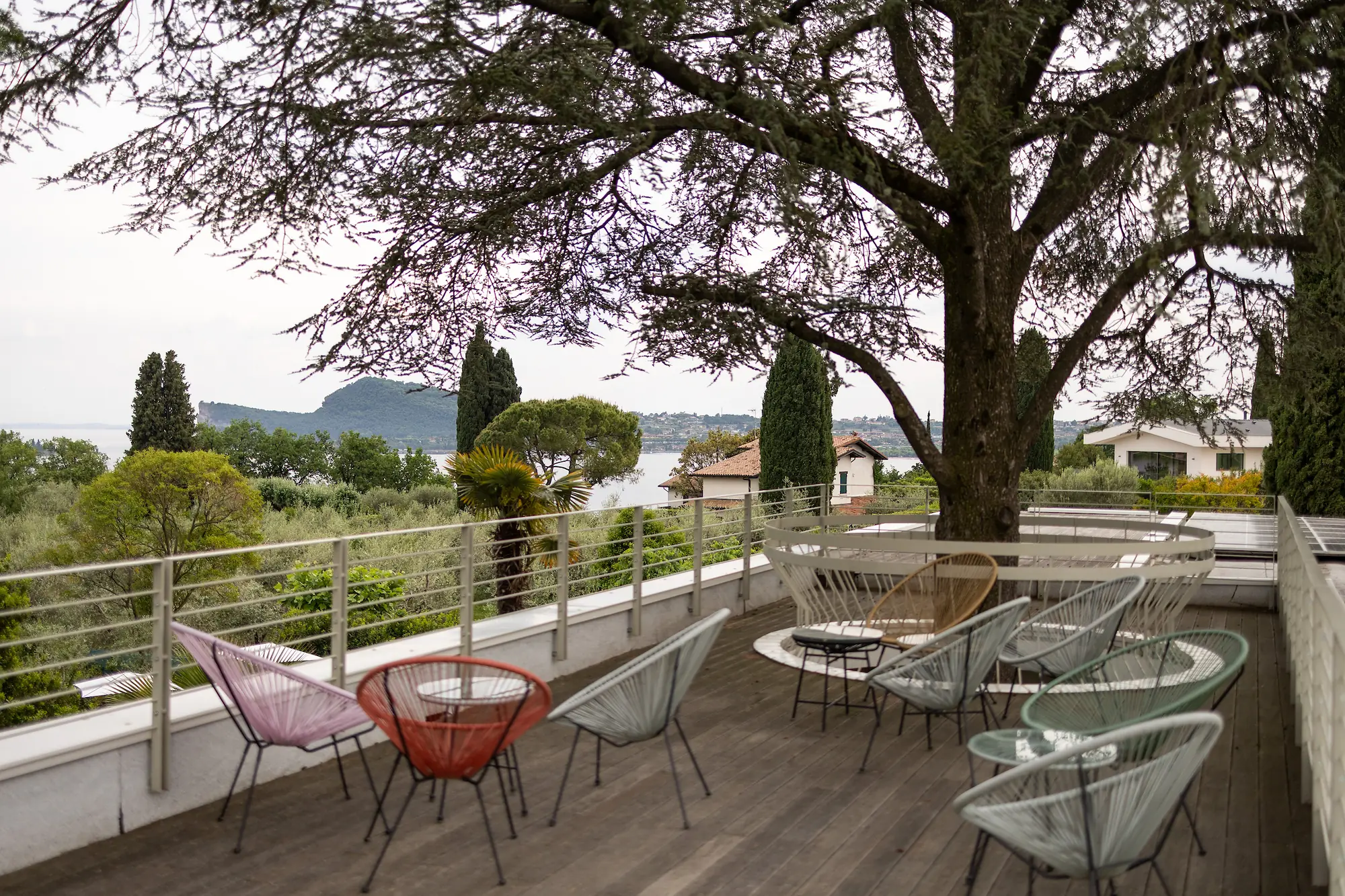 The Iroko-wood roof terrace in the shade of the cedar, with Acapulco chairs and views of Lake Garda