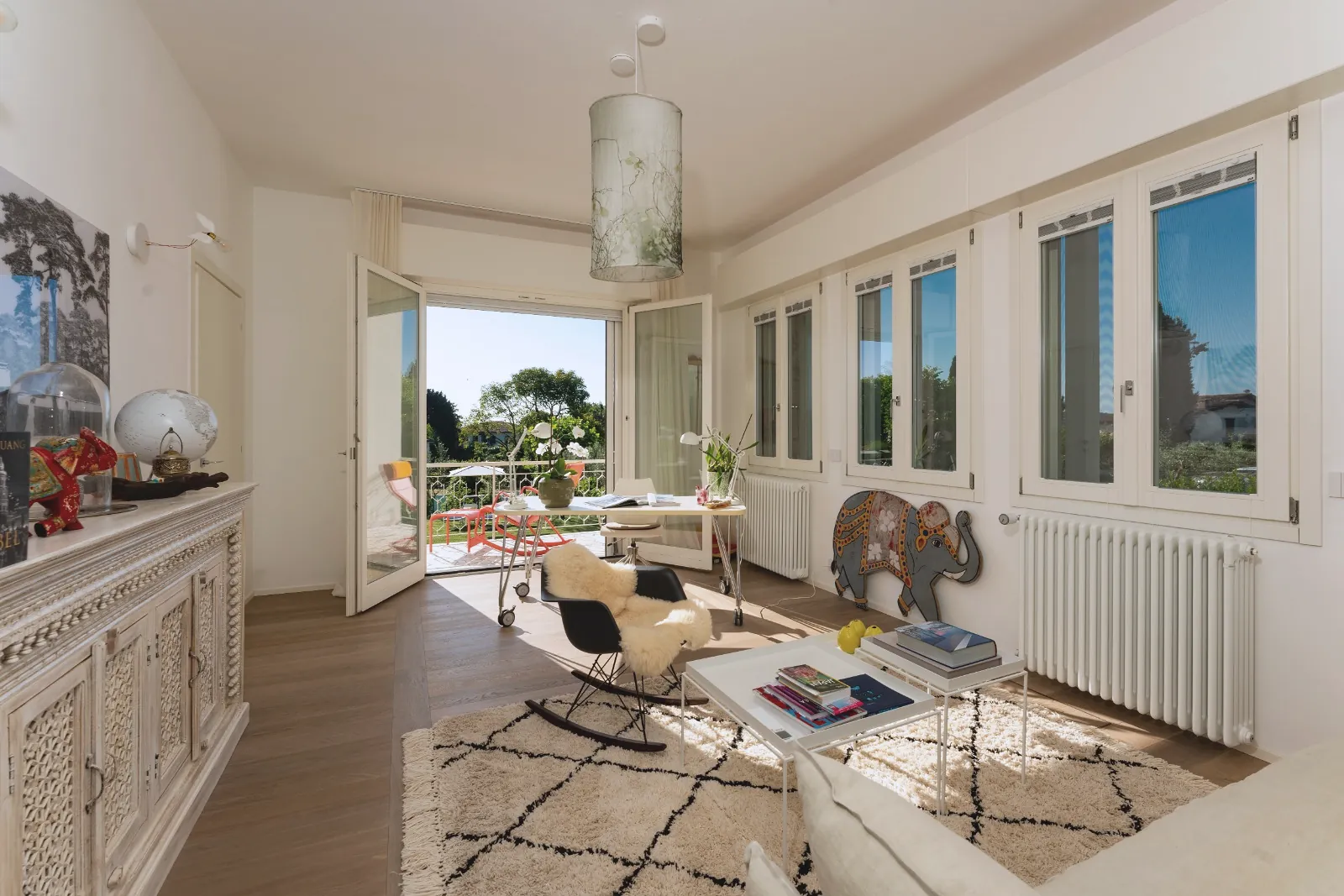 The study with a writing desk by the French doors to the balcony, a rocking chair with sheepskin, a Berber rug and a carved sideboard