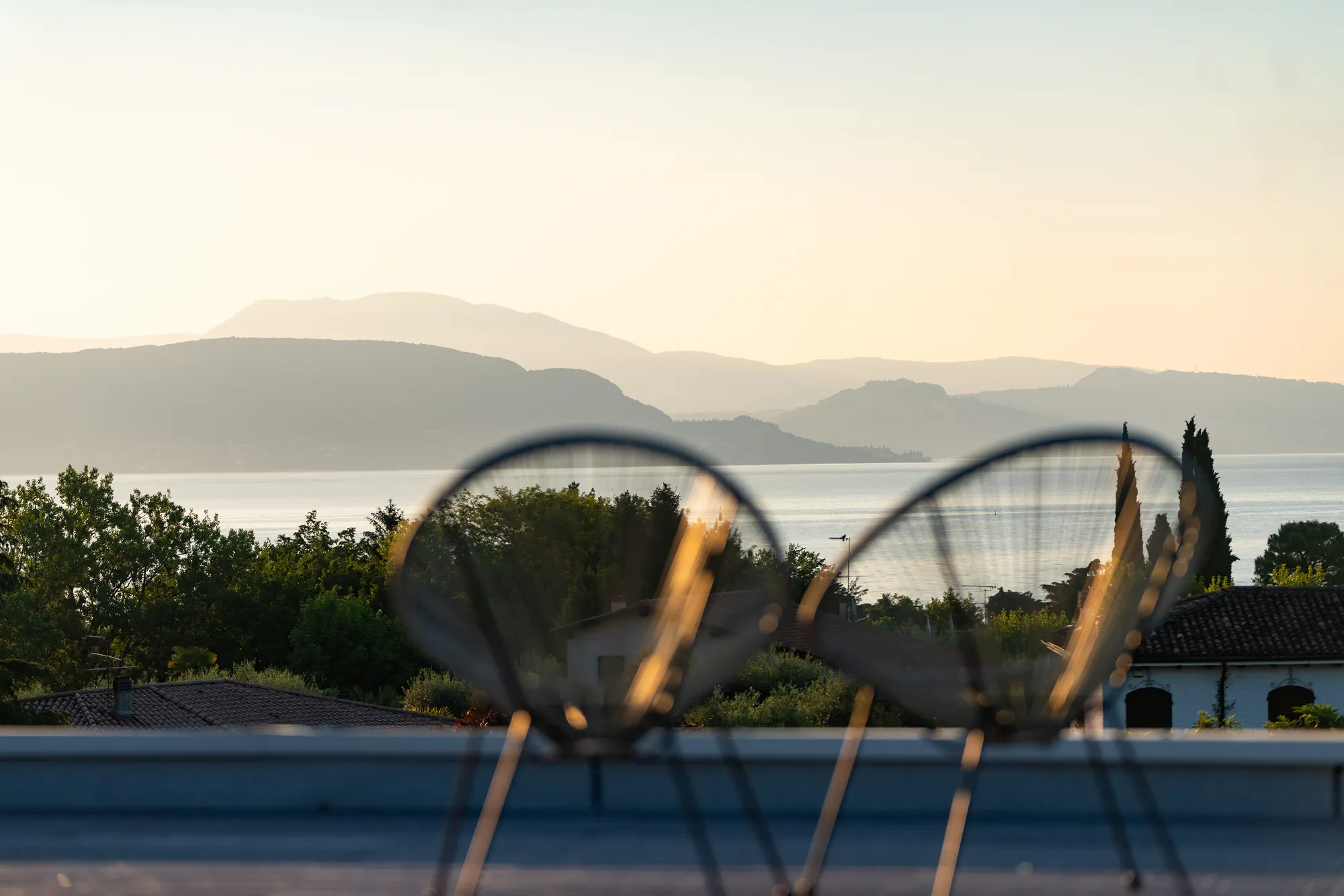 An Acapulco chair silhouetted against a hazy sunset over Lake Garda from the roof terrace