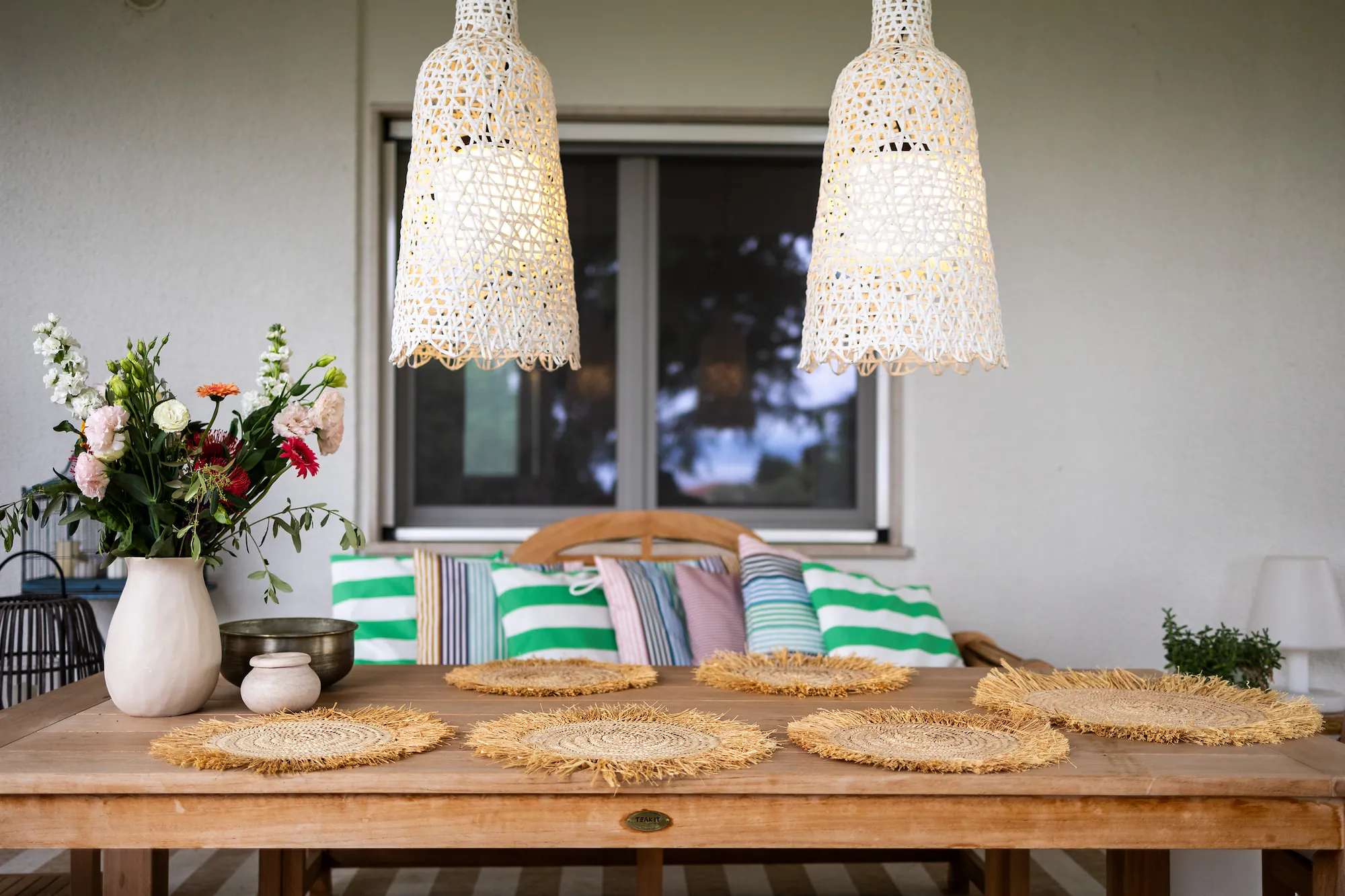 Long teak table with woven placemats under white crochet pendant lamps