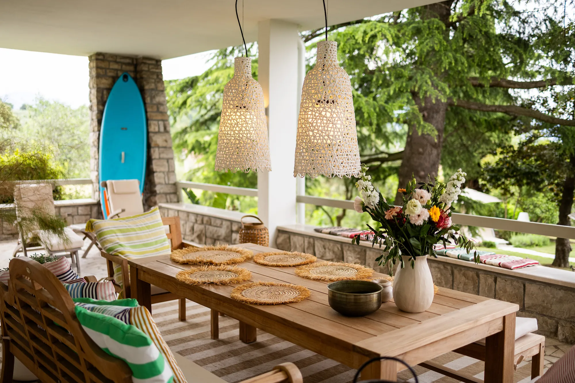 Terrace dining area with a blue surfboard, teak chairs and a view of the garden