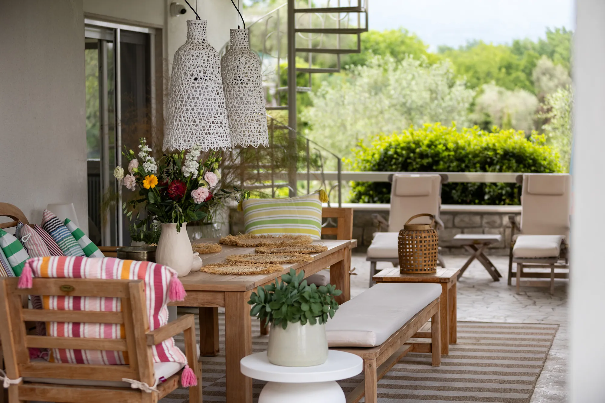 Teak dining table set for lunch with fresh flowers and striped cushions on the main terrace