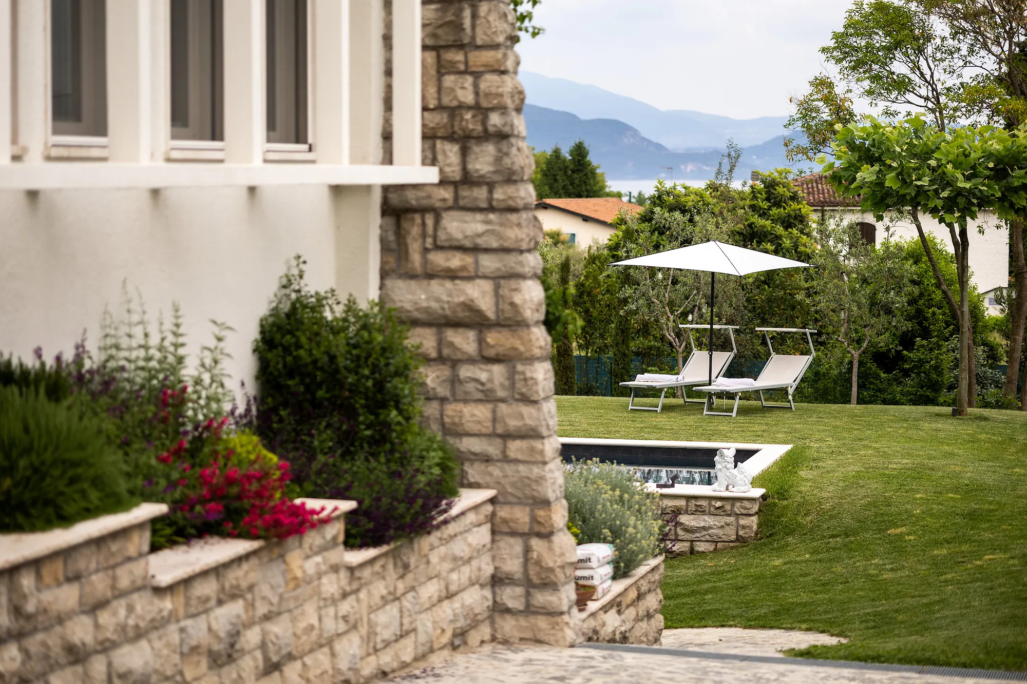 Stone corner of the villa with a view across the garden and pool to Lake Garda