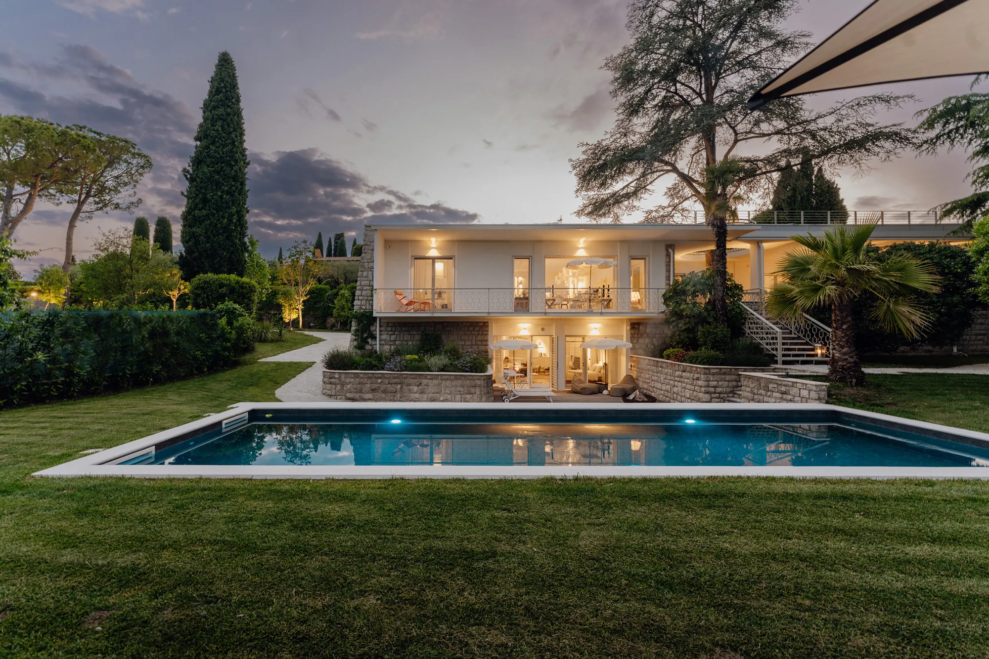 Tree House Lake Garda at dusk, warm lights in the windows reflected in the pool under the cedar